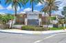 Community entrance featuring stacked-stone masonry, a built-in water feature, manicured landscaping, and mature palm trees