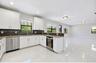 Kitchen featuring white shaker-style cabinetry, stone countertops, a dark-toned tile backsplash, stainless steel appliances, and polished tile floorin