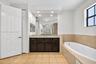 Bathroom featuring a dark-finish vanity, stone-pattern countertop, recessed lighting, wall-to-wall mirror, and a jetted soaking tub with tile surround