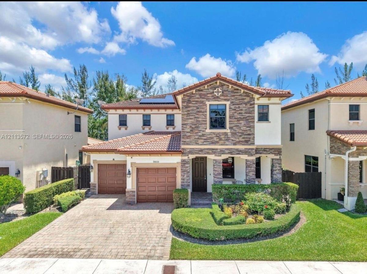 Two-story exterior featuring a stone facade, tile roof, dual-car garage, solar panels, and a paved driveway