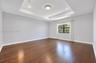 Tray ceiling with recessed lighting, wood-finish flooring, and a single-pane window with a dark frame