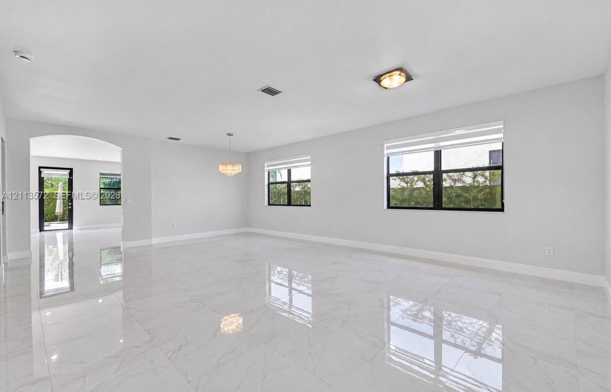Open-concept interior featuring large-format polished tile flooring, black-framed windows, a multi-light chandelier, and an arched entryway