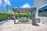 Outdoor patio area featuring a stone-paver surface, a fixed pergola, and a tall privacy hedge
