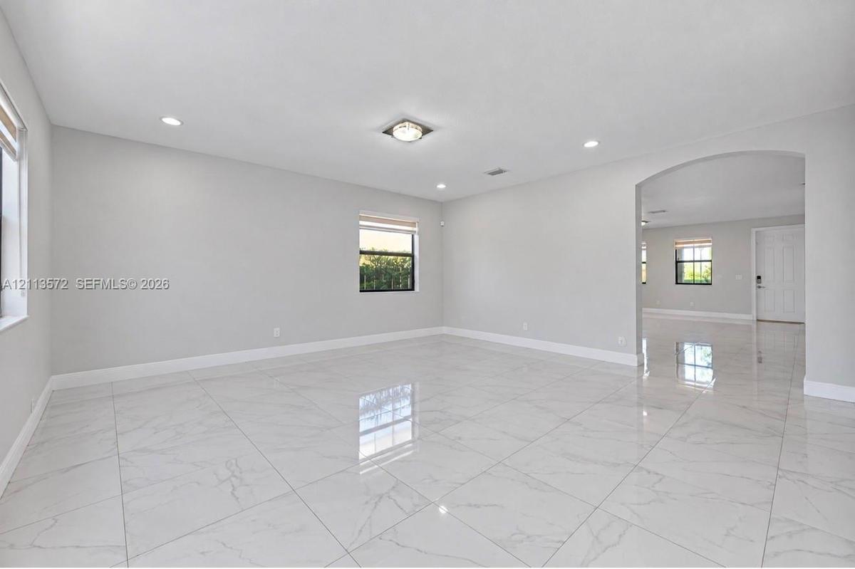 Large-format tile flooring, recessed lighting, archway architectural detailing, and neutral wall tones