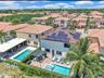 Aerial perspective featuring a two-story residence equipped with roof-mounted solar panels, a rectangular swimming pool, a spillover spa, a stone-pave