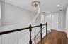 Spiral crystal chandelier with recessed ceiling lighting, wood-finish flooring, and a two-tone railing featuring a dark wood handrail and white balust