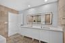 Double vanity with white cabinetry, solid surface countertop, rectangular undermount sinks, tall polished metal faucets, and a large backlit wall-moun