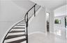 Curved staircase with dark-finished treads and white risers, decorative wood handrail, polished stone flooring, and arched entryway