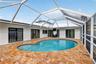 Screened-in patio featuring a custom-shaped pool, natural stone paver deck, multiple glass-paned French doors, and a vaulted enclosure frame