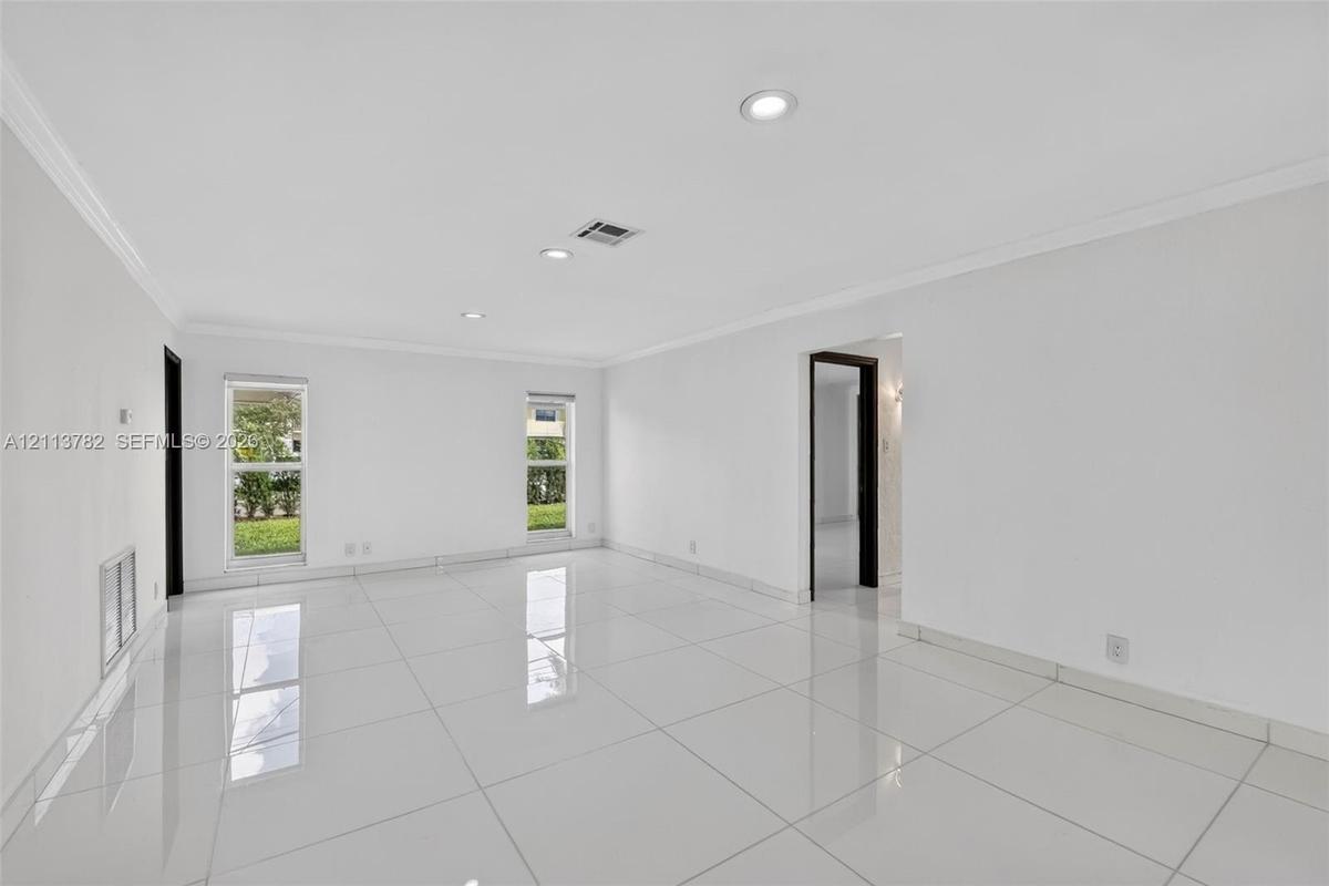 Bright living area featuring large-format polished tile flooring, recessed lighting, crown molding, and dual windows