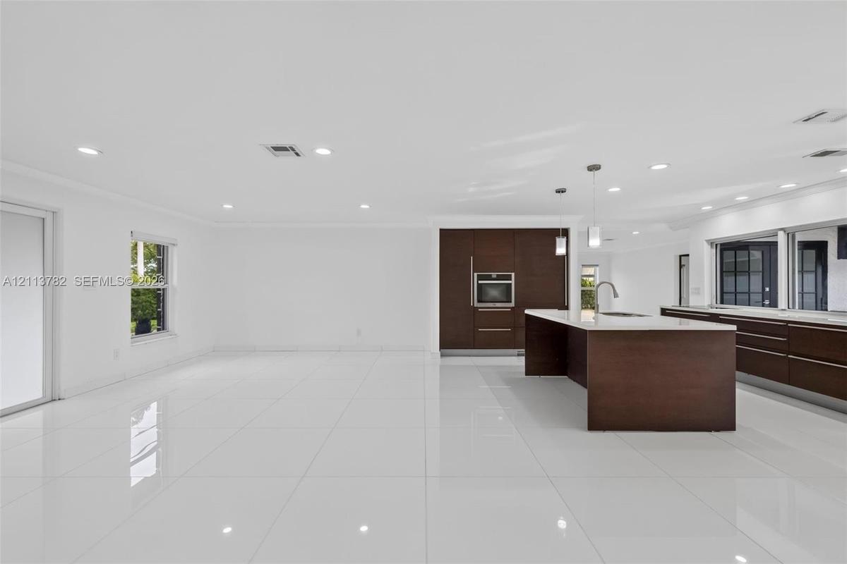 Open-concept kitchen featuring dark wood-finish cabinetry, a large center island with stone-surface countertop, recessed lighting, and white tile floo