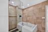Large-format natural stone wall tiling, integrated soaking tub with a white surround, glass shower partition, recessed ceiling lighting, and pebble-st