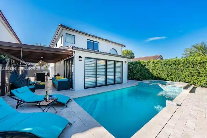 Stucco exterior with multi-panel sliding glass doors, covered patio structure, tiled pool, and raised spa with mosaic tile accents