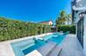 Backyard featuring an inground pool with an integrated spa, stone-finish paver decking, and mature privacy hedging