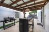 Covered patio featuring a wood-beam pergola, paver flooring, a glass block window, and a hanging pendant light fixture