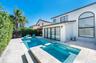 Stucco exterior featuring a multi-panel sliding glass door, arched window, integrated swimming pool with an attached spillover spa, and stone-paver ha