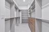 Walk-in closet featuring custom built-in shelving, wood-finish drawer cabinetry, metal hanging rods, and tiled flooring