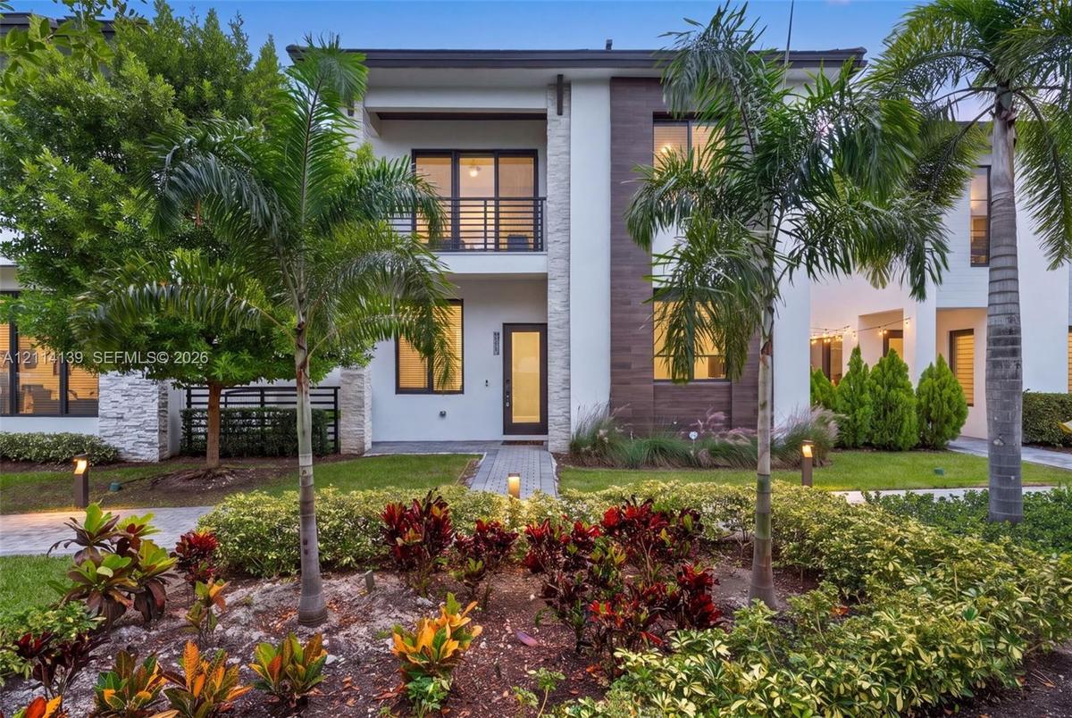 Contemporary two-story exterior featuring smooth stucco siding, stone veneer accents, wood-finish paneling, an upper-level balcony with metal railing,