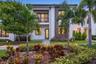 Contemporary two-story exterior featuring smooth stucco siding, stone veneer accents, wood-finish paneling, an upper-level balcony with metal railing,