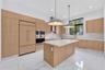 Kitchen featuring wood-finish cabinetry, quartz countertops, an oversized center island, built-in stainless steel appliances, and large-format tile fl