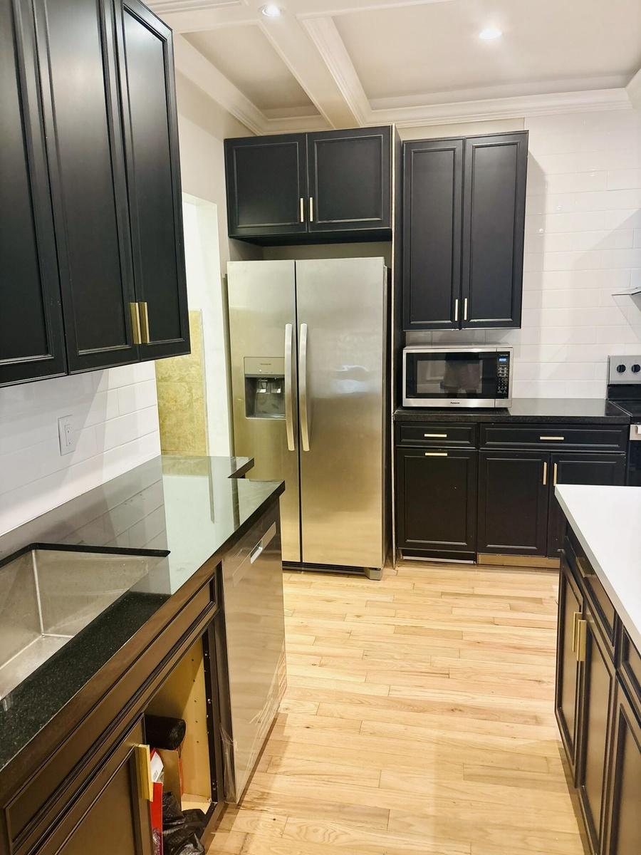 Kitchen featuring shaker-style cabinetry with gold-toned hardware, stainless steel appliances, dark stone-finish countertops, wood-finish flooring, an