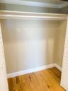 Reach-in closet featuring wood-finish flooring, white louvered doors, and a built-in overhead storage shelf with an integrated hanging rod