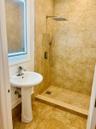 Bathroom featuring a walk-in shower with large-format tile surround, rainfall showerhead, handheld sprayer, and matching tile flooring, complemented b