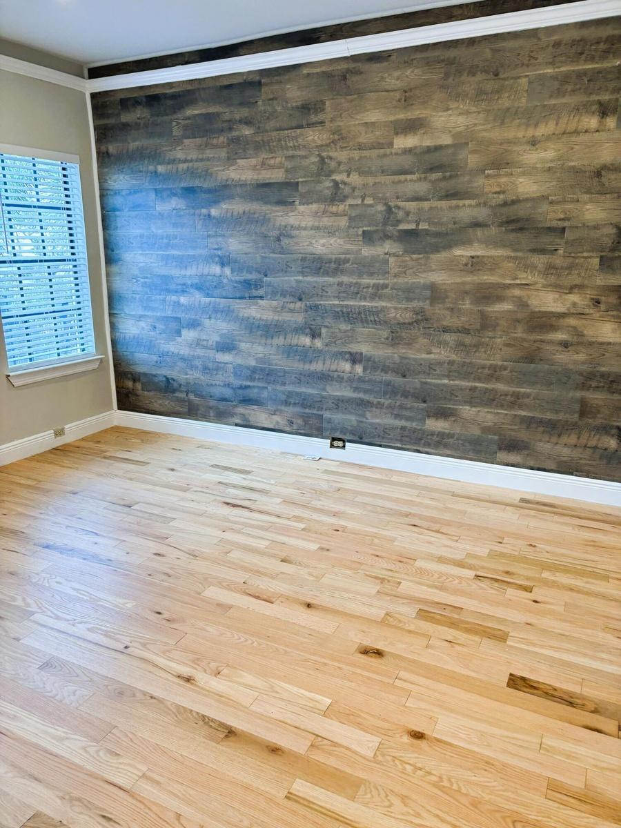 Wood-plank accent wall featuring a rustic finish, light-toned wood-finish flooring, and multi-pane window with interior shutters