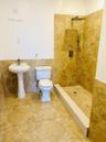 Walk-in shower featuring earth-tone stone tile surround, pebble-texture flooring, and a rainfall showerhead with a handheld sprayer, complemented by a