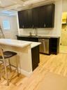 Kitchen featuring custom dark-toned cabinetry, quartz countertops, stainless steel undermount sink with goose-neck faucet, integrated dishwasher, and 