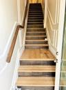 Staircase featuring dual-tone wood treads, wall paneling with decorative trim, and a wall-mounted wooden handrail