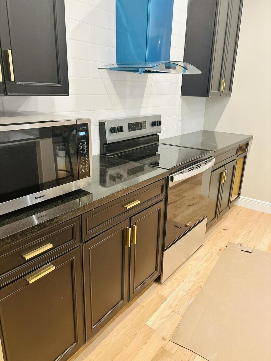 Kitchen featuring dark cabinetry with brass-tone pulls, stone countertops, horizontal tile backsplash, and stainless steel appliances, including a ran
