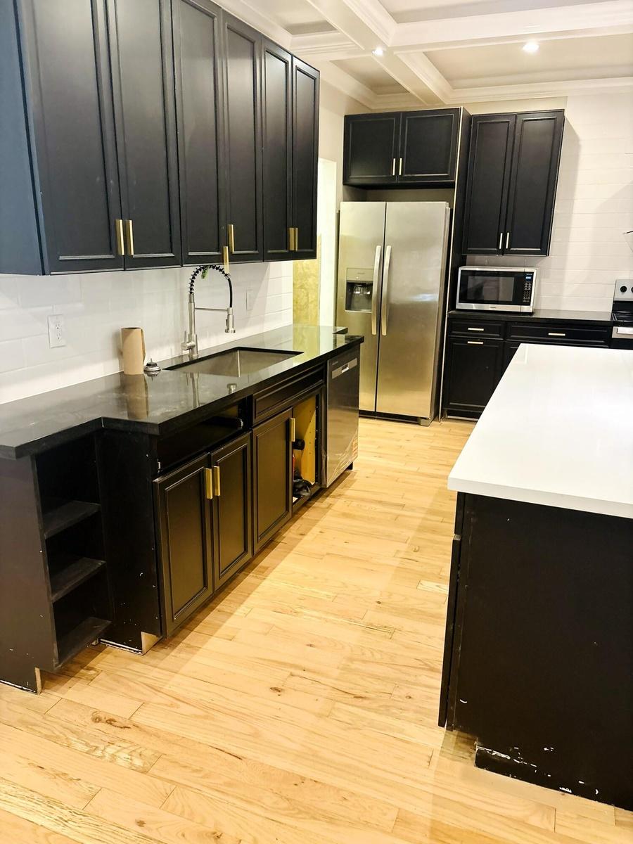 Kitchen featuring matte black cabinetry with gold-tone hardware, wood-finish flooring, quartz countertops, a stainless steel undermount sink with a pu