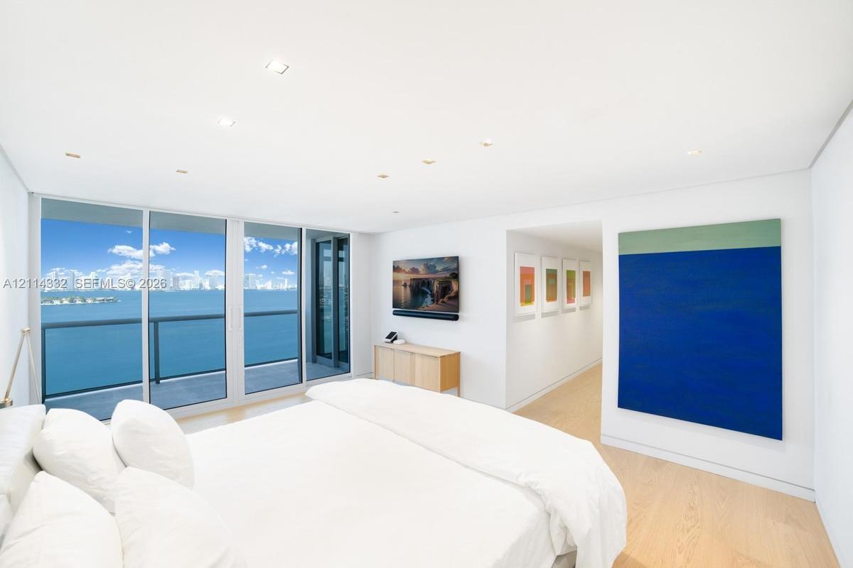 Floor-to-ceiling glass panel windows, private balcony access, recessed ceiling lighting, and light-toned wood-finish flooring