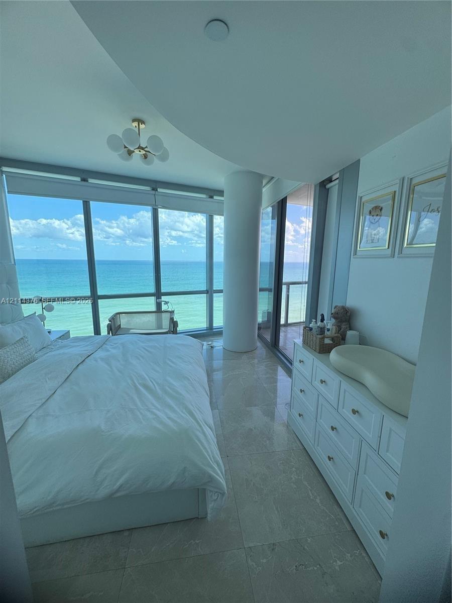 Floor-to-ceiling windows, stone tile flooring, multi-light gold-finish flush mount fixture, and structural cylindrical column