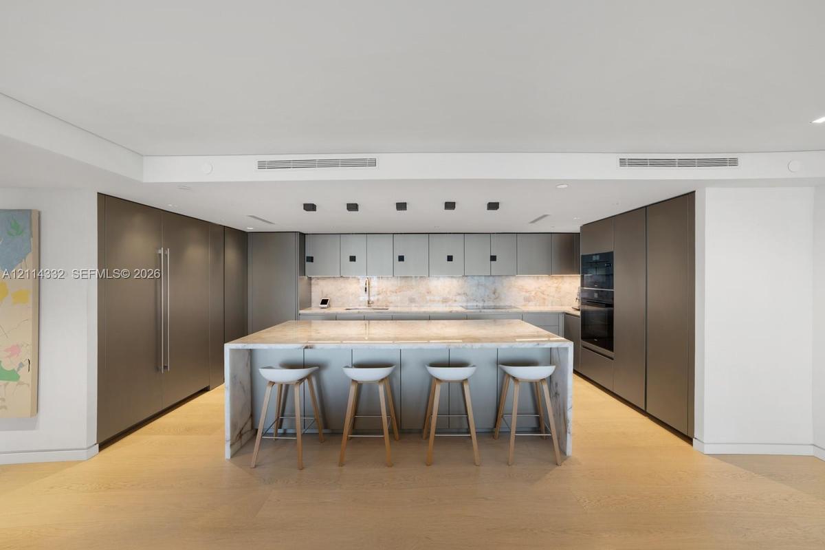 Modern kitchen featuring flat-panel cabinetry, a waterfall-edge stone island, stone backsplash, built-in double wall ovens, and wood-finish flooring