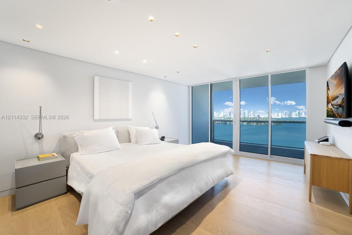 Floor-to-ceiling sliding glass doors, light wood-finish flooring, recessed ceiling lighting, and expansive water and skyline scenery