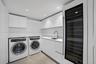 Modern laundry room featuring sleek white cabinetry, solid surface countertops, an integrated wine refrigerator, a stainless steel sink with a high-ar