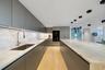 Sleek, handleless grey cabinetry, stone countertops with waterfall edge island, under-cabinet lighting, stainless steel undermount sink with arched fa
