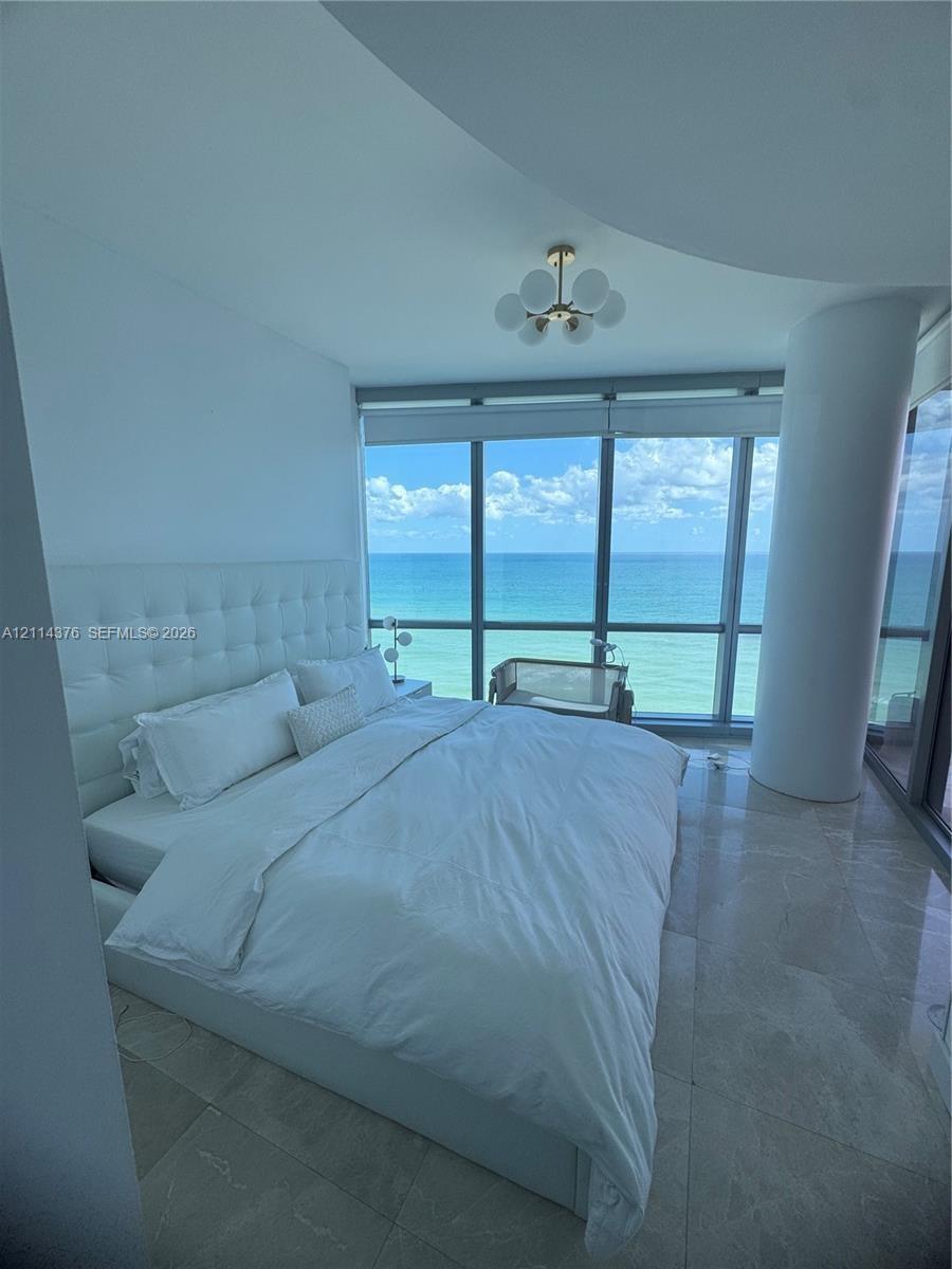 Floor-to-ceiling windows featuring ocean scenery, stone flooring, a structural column, and a multi-globe light fixture