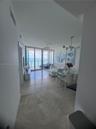 Large-format tile flooring, multi-globe metallic chandelier, floor-to-ceiling glass paneling, and an external balcony featuring a glass railing with a