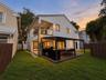 Exterior features include a stucco finish, covered deck with a pergola, built-in outdoor kitchen, second-story balcony with glass railing, and a fence