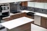 Kitchen featuring wood-finish cabinetry, white countertops, a dark stone backsplash, a black farmhouse-style sink with a matte black faucet, and stain
