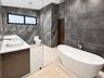 Freestanding white soaking tub with wall-mounted polished chrome faucet, dual vessel sinks atop a wood-finish vanity, and floor-to-ceiling textured st
