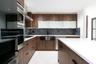 Kitchen featuring wood-finish cabinetry, white countertops, a central island, integrated stainless steel appliances, and a dark stone tile backsplash