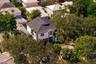 Aerial perspective of a multi-story residence featuring a shingled hipped roof, light-toned exterior finish, attached garage, and mature tree canopy t