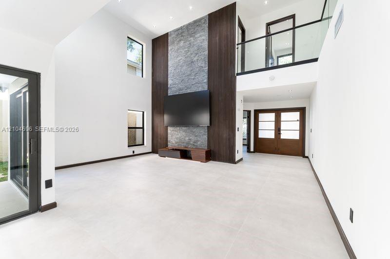 Double-height living area featuring a stone-clad fireplace accent wall, vertical wood-slat detailing, large-format tile flooring, and a glass-paneled 