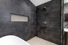 Walk-in shower with dark large-format tile surround, integrated horizontal niche, fixed shower head, and neutral grid-patterned floor tile