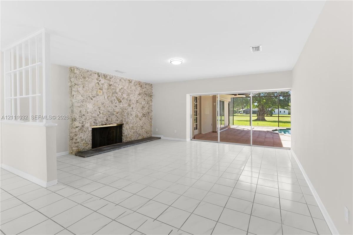 Living area featuring tile flooring, a floor-to-ceiling stone fireplace, a partial-height decorative room divider, and sliding glass doors opening to 