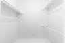 Storage closet featuring tiered white shelving and dual integrated hanging rods